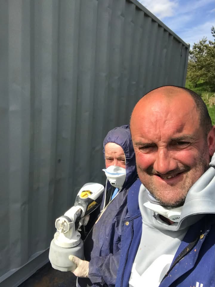 Two members in protective gear spray-painting the beekeepers' container